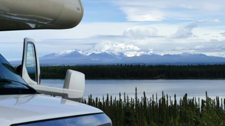 Blick über die Motorhaube eines Wohnmobils auf die St. Elias Mountains und einen See, der von Wald umsäumt ist